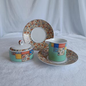 Puede incluir: Un juego de tazas de té y platillos de porcelana coloridos con un diseño de patchwork. El juego incluye una jarra de crema, un azucarero y un platillo con una taza de té.