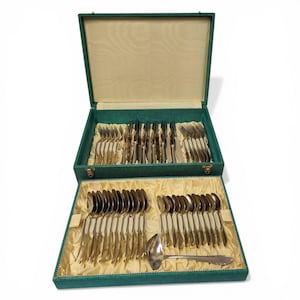 Puede incluir: Un juego completo de cubiertos de plata en un estuche forrado de terciopelo verde. El juego incluye tenedores, cuchillos, cucharas y un cucharón. Los cubiertos plateados están ordenados dentro del estuche abierto, que tiene un interior color crema.