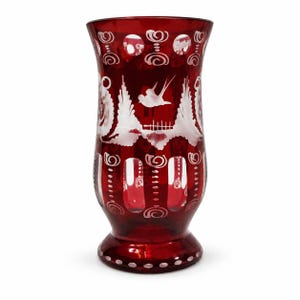 Könnte beinhalten: Eine tiefrote Glasvase mit detaillierten weißen Ätzungen, die einen fliegenden Vogel, stilisierte Blumenmuster und vertikale ovale Ausschnitte zeigen. Das Glas hat einen ausgestellten Rand und einen runden Fuß mit dekorativen weißen Wirbeln.