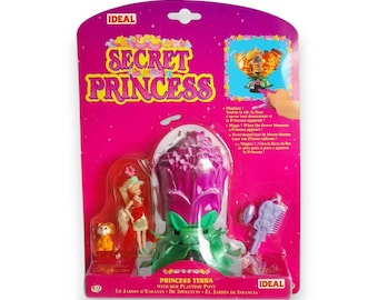 May include: A Secret Princess toy set in a sealed pink package. The packaging features the words "Secret Princess" in yellow. The set includes a doll, a small animal figure, and a flower-shaped playset. The brand name "Ideal" is visible on the packaging.