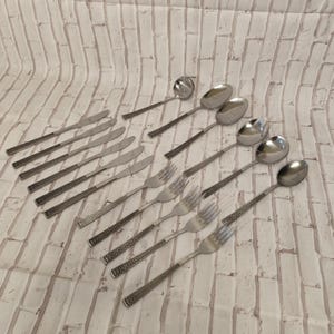 Può includere: Un set di posate in acciaio inossidabile con coltelli, forchette, cucchiai e un mestolo. I manici hanno un motivo decorativo. Il set include più pezzi per un'esperienza culinaria completa.