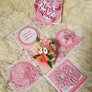 Könnte beinhalten: Eine rosa und weiße Explosionsbox-Karte mit einem 3D-Blumenarrangement, einem Schmetterling und dem Text "Happy Birthday" und "Man wird nicht älter, sondern besser!" Die Box ist mit Spitze und Glitzer verziert.