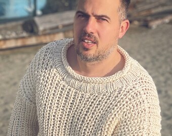 May include: A cream-coloured knitted jumper with a loose fit and a wide, ribbed neckline.