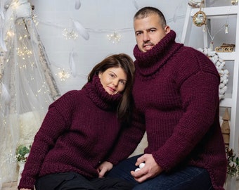 May include: Two individuals wearing matching deep burgundy, chunky knit sweaters with high, thick turtleneck collars. The sweaters feature long sleeves and a textured, heavy yarn construction, providing a uniform look for both people.