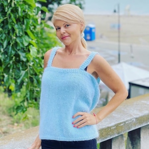 May include: A light blue knitted tank top with thin straps. The tank top is made of a soft, fuzzy yarn.