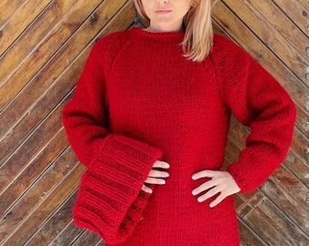 May include: A vibrant red long-sleeve sweater crafted from thick, chunky knit yarn. The garment features a classic crew neckline, raglan sleeves, and prominent, wide ribbed cuffs that extend past the wrists, creating a distinct textured look.