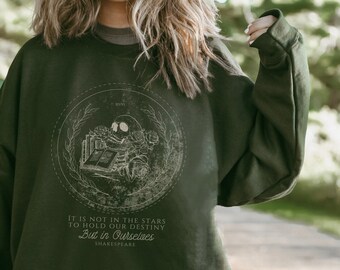 May include: A dark green sweatshirt with a white graphic print of a skull holding a book. The graphic is surrounded by a wreath of leaves and roses. The text below the graphic reads "It is not in the stars to hold our destiny But in Ourselves Shakespeare."