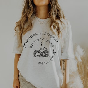 May include: White oversized t-shirt with a graphic of a snake and the text "protectress and fighter breaker of generational curses".