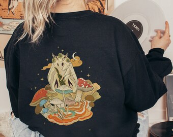 May include: Black sweatshirt with a graphic print of a moth with a crown and mushrooms on a dark background. The graphic is in a vintage style with a moon and stars.