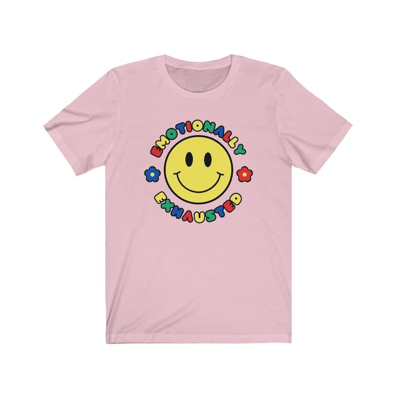 May include: Pink short-sleeved t-shirt with a yellow smiley face in a circle. The circle has the text "Emotionally Exhausted" around the smiley face in rainbow colors.