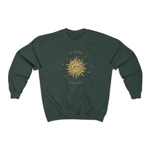 Peut inclure: Un sweat-shirt vert fonc&eacute; avec un motif soleil et lune dor&eacute;. Le soleil a un visage et est entour&eacute; d'&eacute;toiles. Le texte "LE SOLEIL" est au-dessus du soleil et "LA LUNE" est en dessous du soleil.
