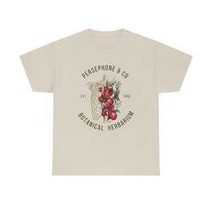 May include: A beige t-shirt with a graphic print of a skeleton with flowers and pomegranates inside the ribcage. The text "PERSEPHONE & CO. EST. 1989 BOTANICAL HERBARIUM" surrounds the graphic.