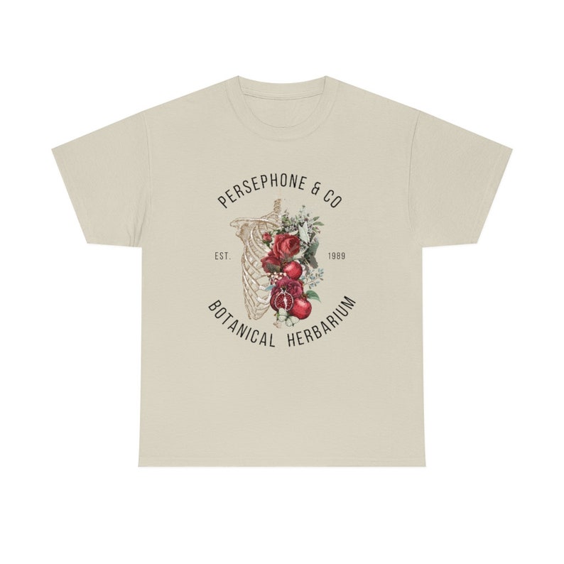 May include: A beige t-shirt with a graphic print of a skeleton with flowers and pomegranates inside the ribcage. The text "PERSEPHONE & CO. EST. 1989 BOTANICAL HERBARIUM" surrounds the graphic.