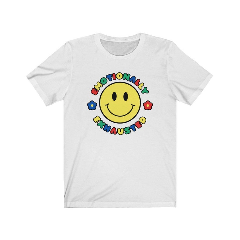 May include: White t-shirt with a yellow smiley face surrounded by the text "Emotionally Exhausted" in a colorful circle.