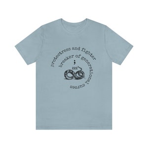 May include: Light blue t-shirt with a circular design featuring a snake, the text "protectress and fighter breaker of generational curses", and the number "222".