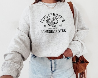 Peut inclure: Sweat-shirt gris avec un imprimé graphique noir de grenades et le texte "Persephone's Farm Fresh Pomegranates" avec les chiffres 19 et 46.