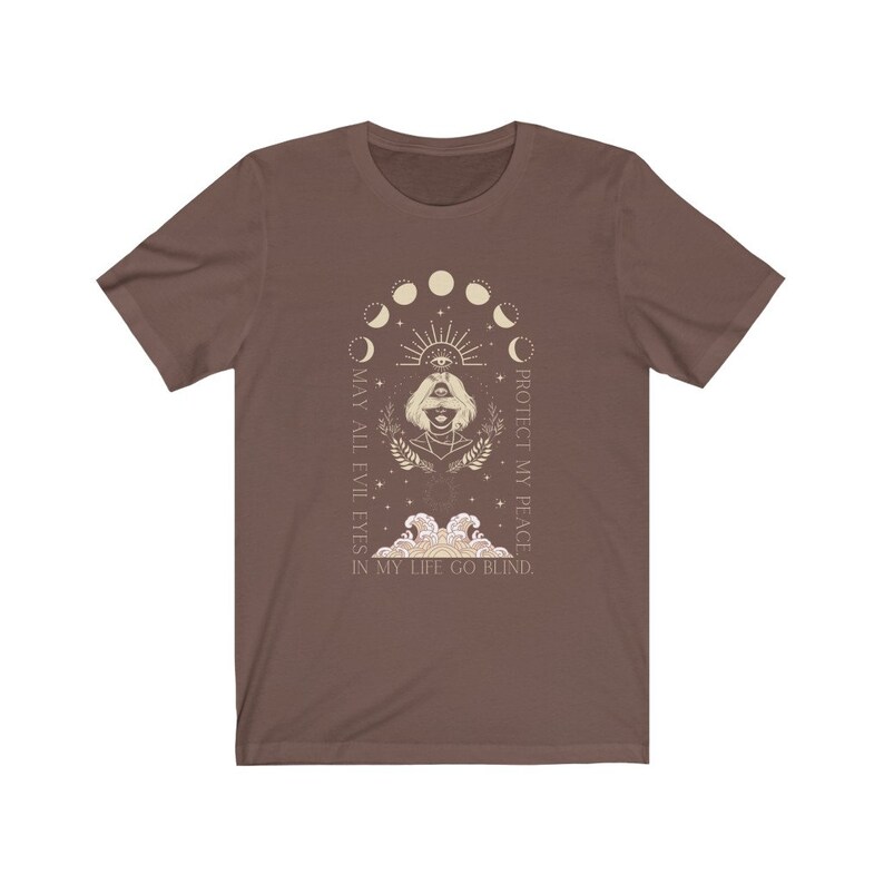 May include: Brown t-shirt featuring a beige graphic with a woman's face, an eye, and moon phases. The text reads "MAY ALL EVIL EYES IN MY LIFE GO BLIND. PROTECT MY PEACE."