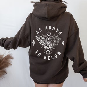 May include: A brown hooded sweatshirt with a white graphic print of a moth, flowers, and the text "As Above So Below".