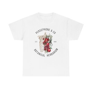 May include: White t-shirt with a graphic design of a skeleton with red roses and pomegranates inside the ribcage. The text "PERSEPHONE & CO. EST. 1989 BOTANICAL HERBARIUM" surrounds the graphic.