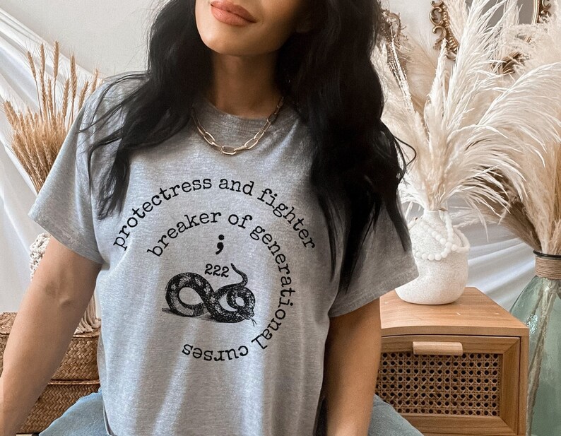 May include: Grey t-shirt with a black snake graphic and the text "protectress and fighter breaker of generational curses 222".