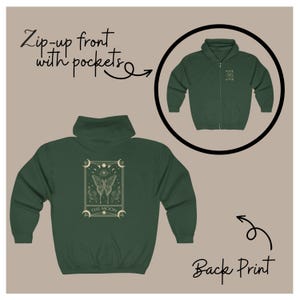 Può includere: Una felpa con cappuccio verde scuro con zip sul davanti e una stampa sul retro di una carta dei tarocchi con una farfalla e le parole "The Moon".