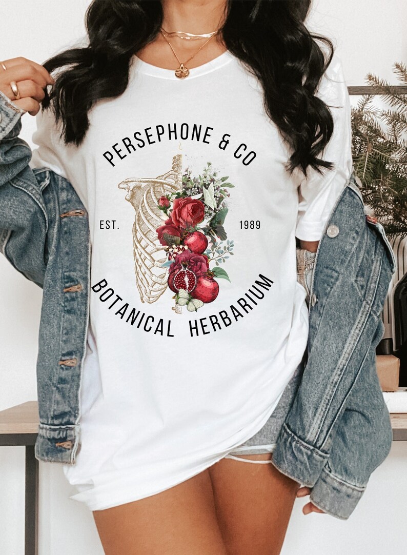 May include: White t-shirt with a floral and skeletal design. The text reads "PERSEPHONE & CO EST. 1989 BOTANICAL HERBARIUM".