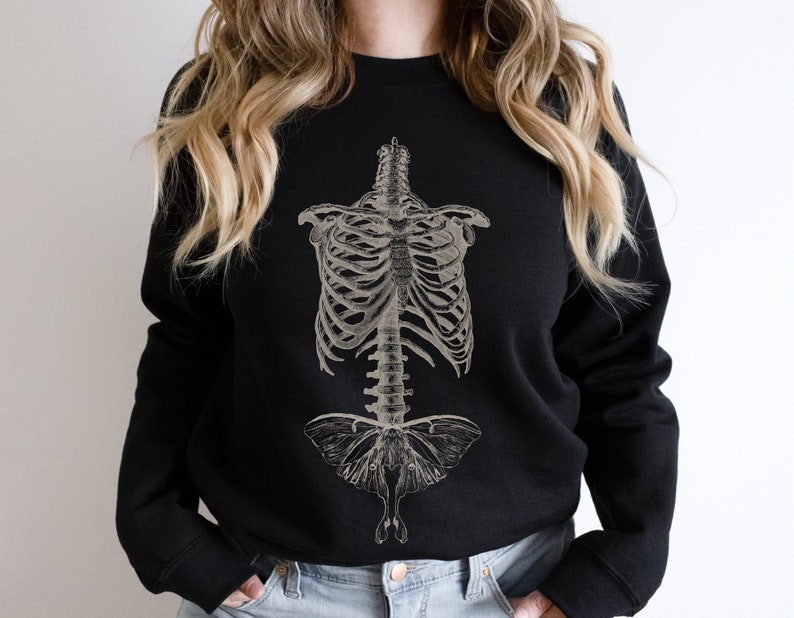 May include: Black sweatshirt featuring a vintage anatomical illustration of a human ribcage and a moth. The moth is centrally positioned and has a detailed design.