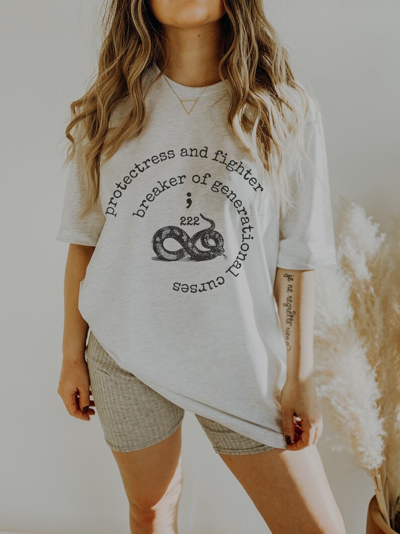May include: White oversized t-shirt with a graphic of a snake and the text "protectress and fighter breaker of generational curses".