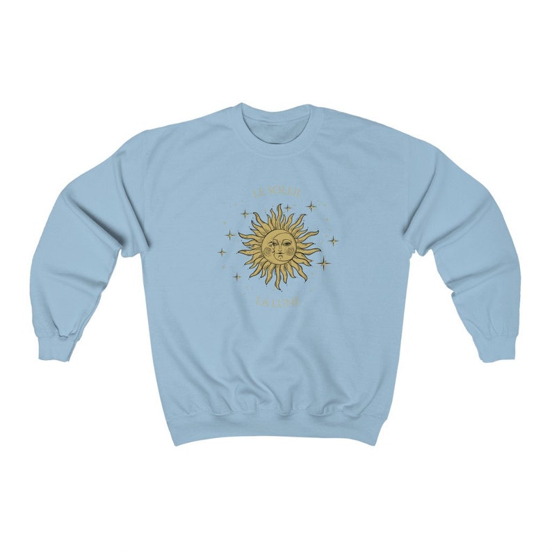 Peut inclure: Sweat-shirt bleu clair avec un motif soleil et &eacute;toiles dor&eacute;s. Le soleil a un visage et est entour&eacute; d'&eacute;toiles. Le texte "The sun always shines" est &eacute;crit autour du soleil.