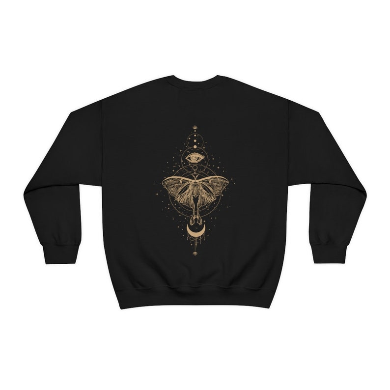 Puede incluir: Sudadera negra con un gr&aacute;fico dorado de una polilla, una luna creciente y un ojo rodeado de estrellas y c&iacute;rculos.