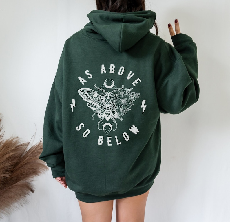 May include: A dark green hooded sweatshirt with a white graphic print on the back. The graphic features a moth with wings spread, a crescent moon, and the text "As Above So Below".