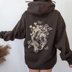 May include: A brown hoodie with a graphic print of a heart surrounded by mushrooms, butterflies, and flowers.