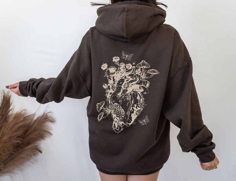 May include: A brown hoodie with a graphic print of a heart surrounded by mushrooms, butterflies, and flowers.