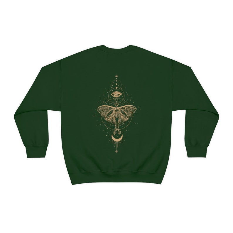 Puede incluir: Una sudadera verde oscuro con un dise&ntilde;o dorado de una polilla con una luna creciente y un ojo en un c&iacute;rculo en la espalda.