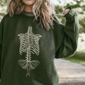 May include: A dark green sweatshirt featuring a vintage illustration of a human ribcage and a moth.