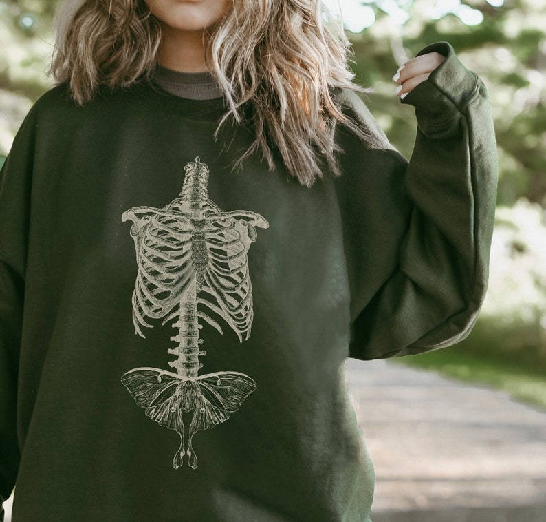 May include: A dark green sweatshirt featuring a vintage illustration of a human ribcage and a moth.