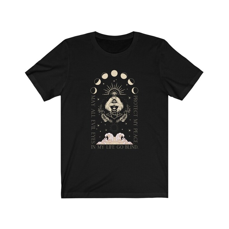 May include: Black t-shirt featuring a mystical design with a woman's face, an eye, and moon phases. The text reads "MAY ALL EVIL EYES IN MY LIFE GO BLIND. PROTECT MY PEACE." The design is in cream and gold tones.