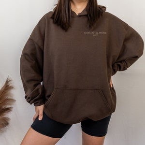 May include: A brown hooded sweatshirt with the text "MEMENTO MORI VIXI" printed on the front.