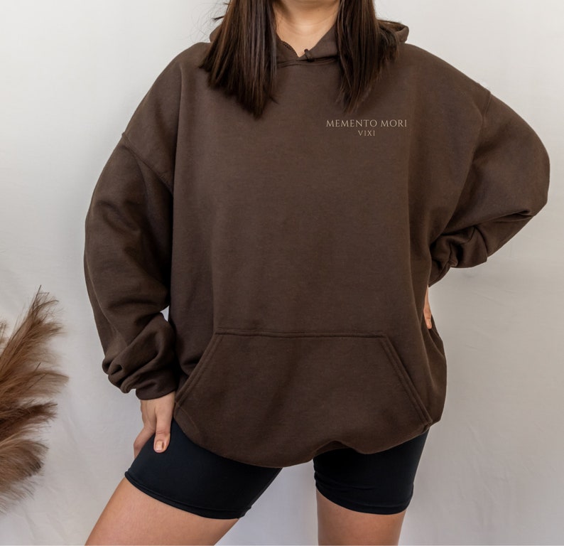 May include: A brown hooded sweatshirt with the text "MEMENTO MORI VIXI" printed on the front.