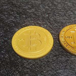 Pu&ograve; includere: Due monete d'oro Bitcoin con il simbolo Bitcoin e il testo "LIBERTAS" e "2000" sulle monete.
