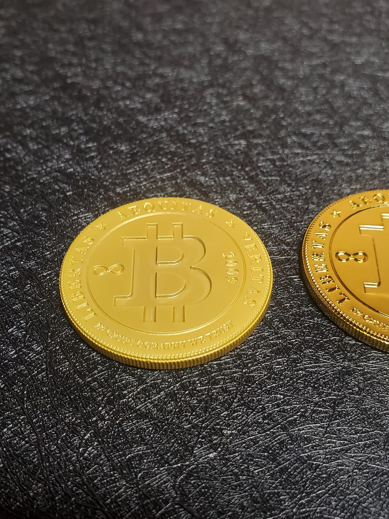 Pu&ograve; includere: Due monete d'oro Bitcoin con il simbolo Bitcoin e il testo "LIBERTAS" e "2000" sulle monete.