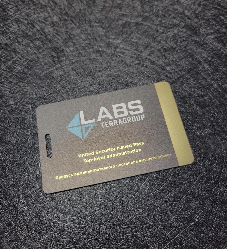 Puede incluir: Una tarjeta de identificaci&oacute;n rectangular con el texto "LABS TERRAGROUP" y un logotipo turquesa y blanco. La tarjeta tambi&eacute;n incluye el texto "United Security Issued Pass Top-level administration" y texto en otro idioma. La tarjeta tiene un borde dorado.