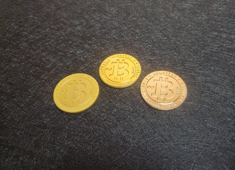 Pu&ograve; includere: Tre monete Bitcoin dorate con il simbolo Bitcoin su ciascuna. Le monete sono su una superficie nera.