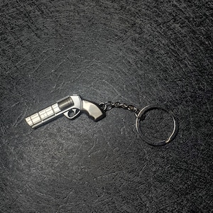 May include: A silver-colored keychain shaped like a pistol with a chain and a circular ring.