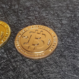 Pu&ograve; includere: Moneta Bitcoin dorata con il testo "LIBERTAS & AQUILA" e "VERITAS" sul bordo.