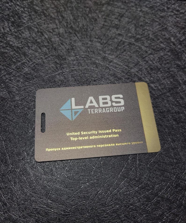 Puede incluir: Una tarjeta de identificaci&oacute;n rectangular gris con el texto "LABS TERRAGROUP" y un logotipo azul y blanco. La tarjeta tambi&eacute;n incluye el texto "United Security Issued Pass Top-level administration" y texto en otro idioma.