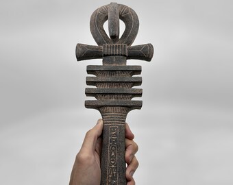 以下が含まれることがあります： 複雑な彫刻とヒエログリフが施された、濃い茶色の木製アンク。古代エジプトの生命の象徴です。アンクは手に持たれており、その大きさや細部がわかります。
