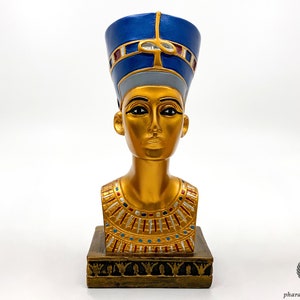 Könnte beinhalten: Goldene Büste einer ägyptischen Königin mit einer blauen und goldenen Krone. Die Büste steht auf einem goldenen Sockel mit aufwendigen Details.