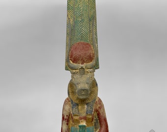 May include: A wooden statue of an Egyptian god with a bull's head, wearing a green and red headdress with a sun disk. The statue is painted in shades of brown, green, red, and blue.