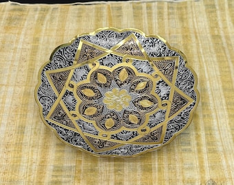 Könnte beinhalten: Eine dekorative Metallschale mit einer goldenen, silbernen und kupfernen Oberfläche. Die Schale zeigt ein kompliziertes Design aus einem Stern und einer Blume.